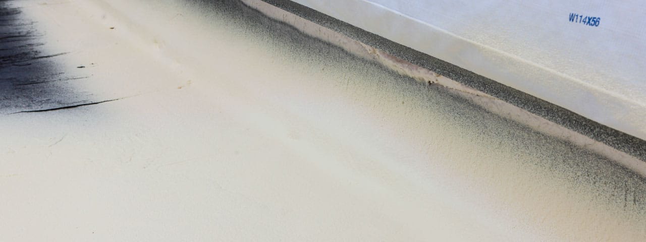 Spray foam roofing self-flashed around a parapet wall on a Kansas City commercial building